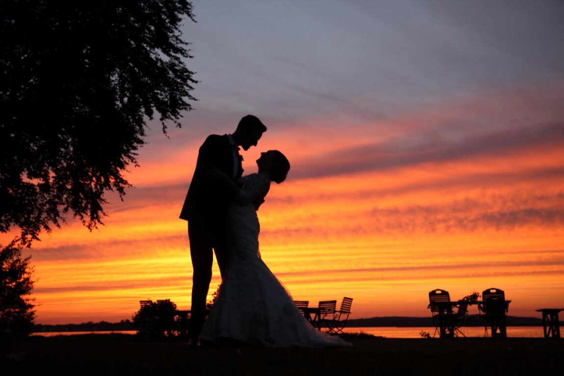 Hochzeitsfotografie - Das Brautpaar steht eng umschlungen am Ufer eines Sees.